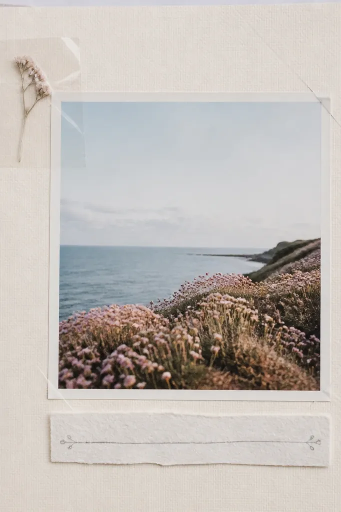 A pastel scrapbook page with a single photo in the center. In the top-left corner, a pressed tiny flower sits under a clear tape square. The tape edges are crisp and glossy. There's minimal journaling in soft gray ink on a narrow strip beneath the photo.