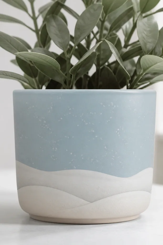 A light blue pot with three layered white snow hill shapes near the bottom, and tiny speckled snow dots across the midsection.