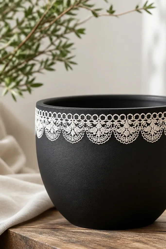 A matte black pot with a white border band near the top that looks like lace patterns, including small loops and scallops.