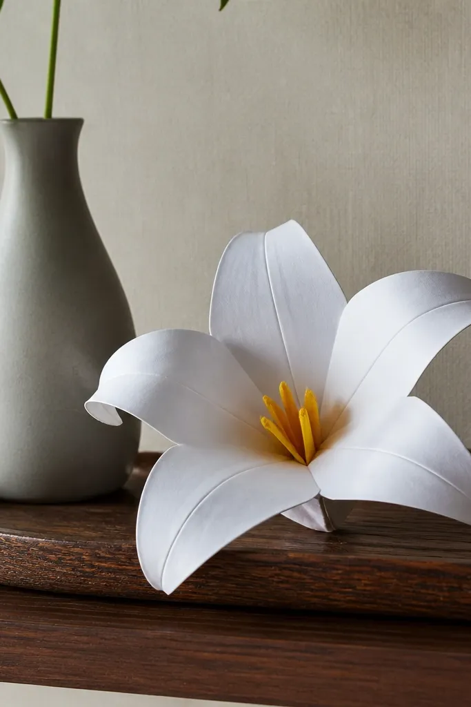 A lily flower with curved petals in white paper and a yellow center