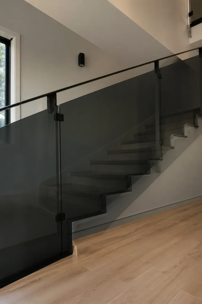 Smoked glass stair railing with thin black rails and a floating wood handrail