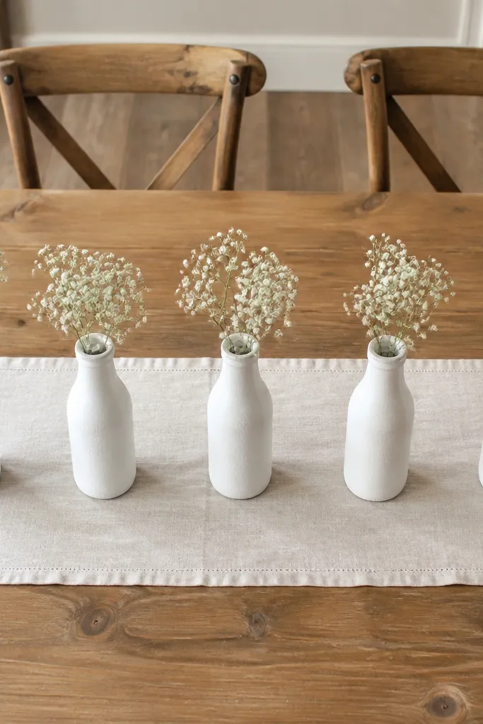Three small chalk-painted bottles holding single stems in a line