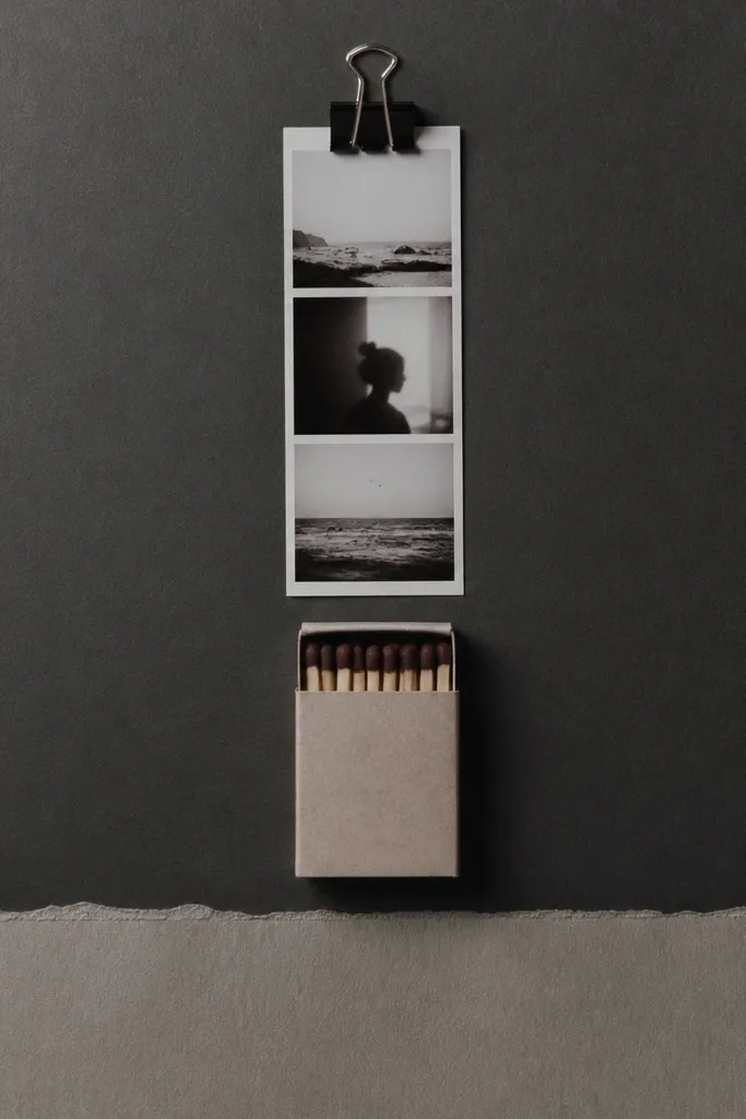 A page with a small matchbook centered vertically. A mini binder clip holds a photo strip at the top. The background is charcoal gray with a lighter gray journaling strip at the bottom.