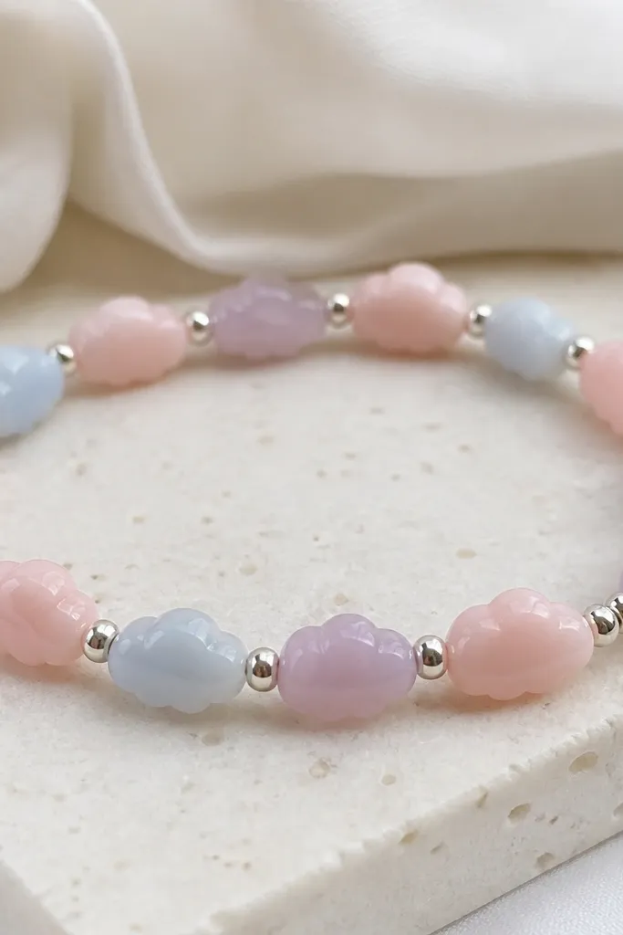Soft pastel beads shaped like tiny rounded clouds in blush pink, powder blue, and lavender, separated by small metallic silver dot beads; the bracelet is muted and airy.