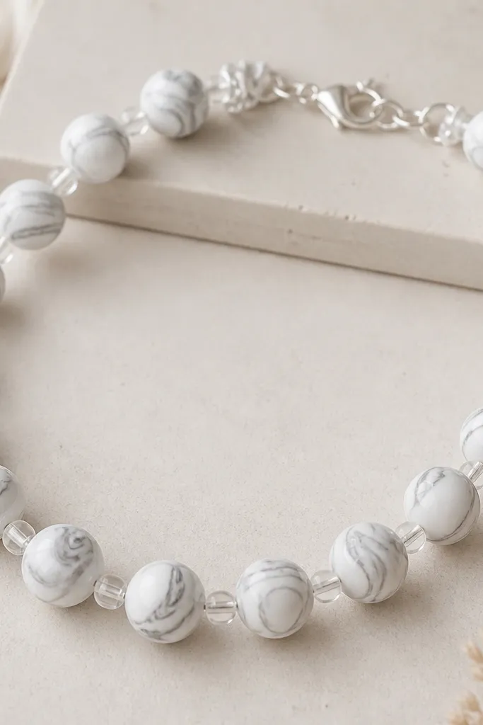 White marbled clay beads with gray swirls, separated by small transparent acrylic spacers and silver jump rings near the clasp.