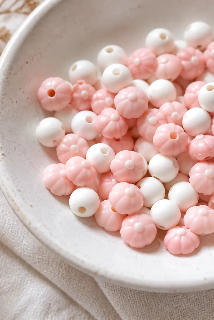Clay beads shaped like tiny flower caps in pink with a small center bump, mixed with smooth white beads.