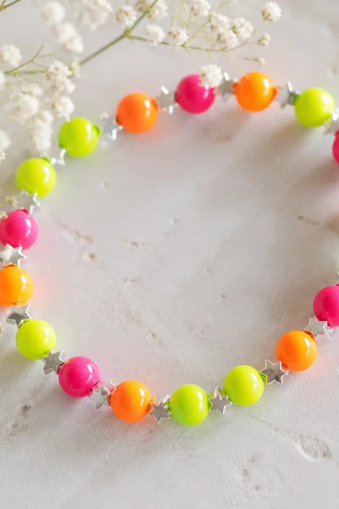 Neon neon beads in lime, hot pink, and bright orange strung on clear elastic, with small star-shaped spacers in silver.