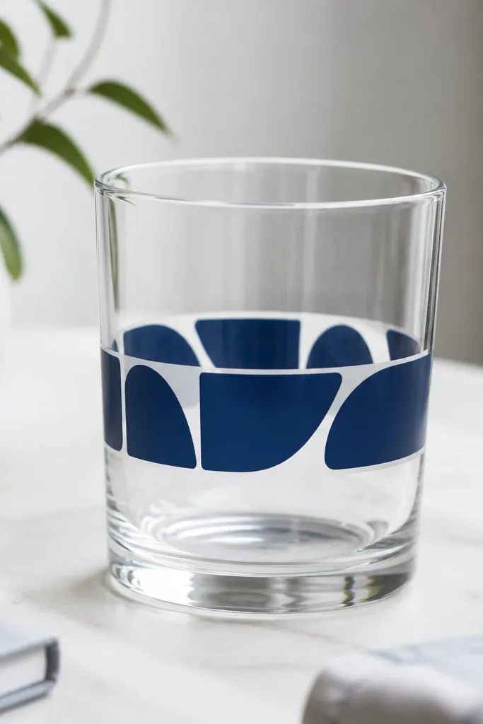 A clear tumbler has a band of stenciled letters wrapped around it, with clean edges and a glossy finish; the band looks like it was printed.