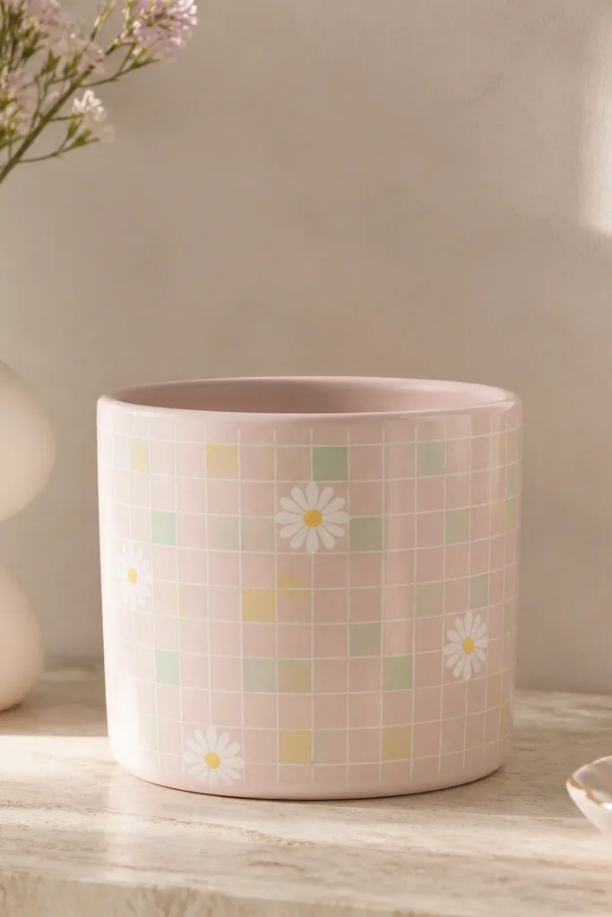 A light pink pot painted with a small checkered grid in white, mint, and pale yellow, with a few tiny white daisies and yellow centers on the front.