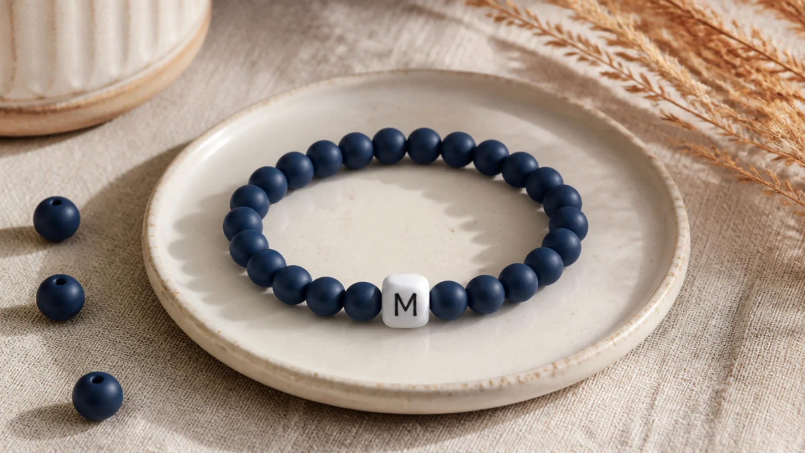 A navy clay bead bracelet with a single white square letter bead showing a monogram initial at the front.