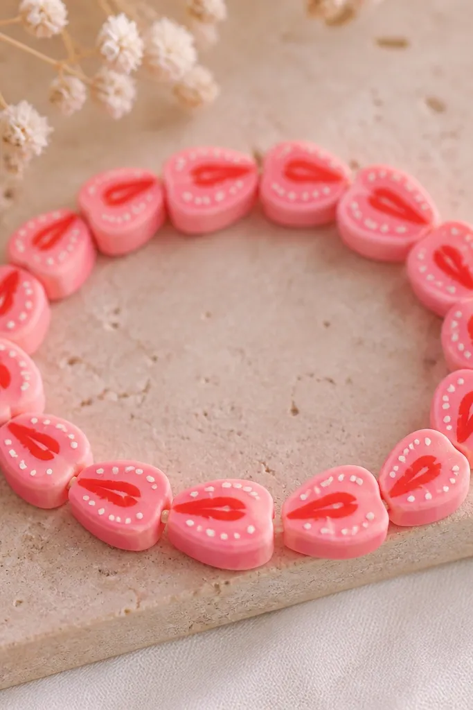Beads shaped like small strawberry slices: pink outer layer with tiny white seed dots and a darker red center stripe; bracelet is on stretchy cord.
