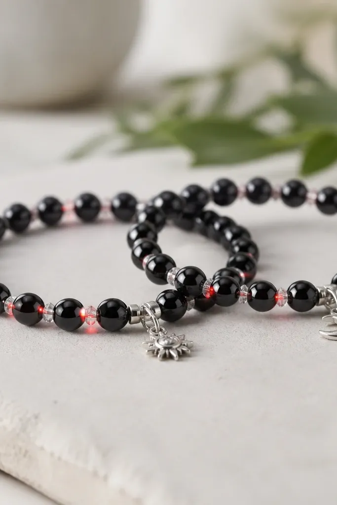 Two matching bracelets with glossy black 8mm clay beads and tiny clear spacer beads. Red LED dots blink through the center line, with a small silver charm at the clasp. The wire is hidden under a black bead cap.