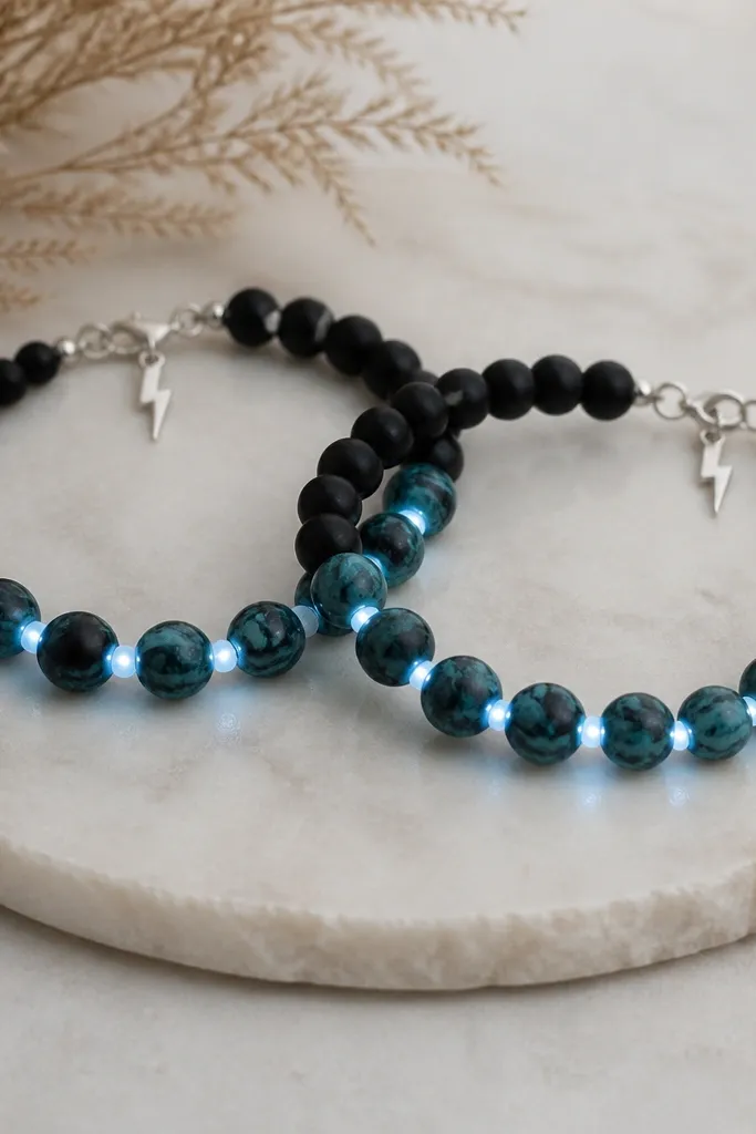 Two bracelets with teal and black marble clay beads. White LEDs run in a slightly zigzag line through the middle beads. A tiny silver lightning charm hangs near the clasp.