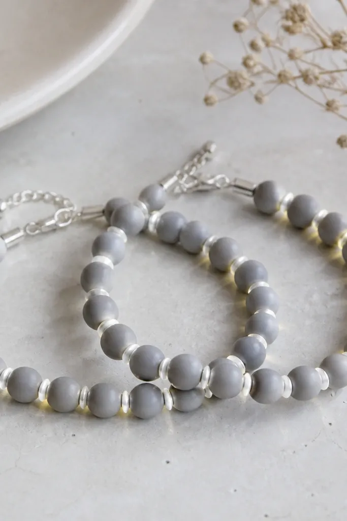 Two bracelets in matte gray clay beads with 8mm size. Silver LEDs run along the edge bead gaps, not the center. The clasp has a thin silver chain extender and a small bead cap covering the wire.