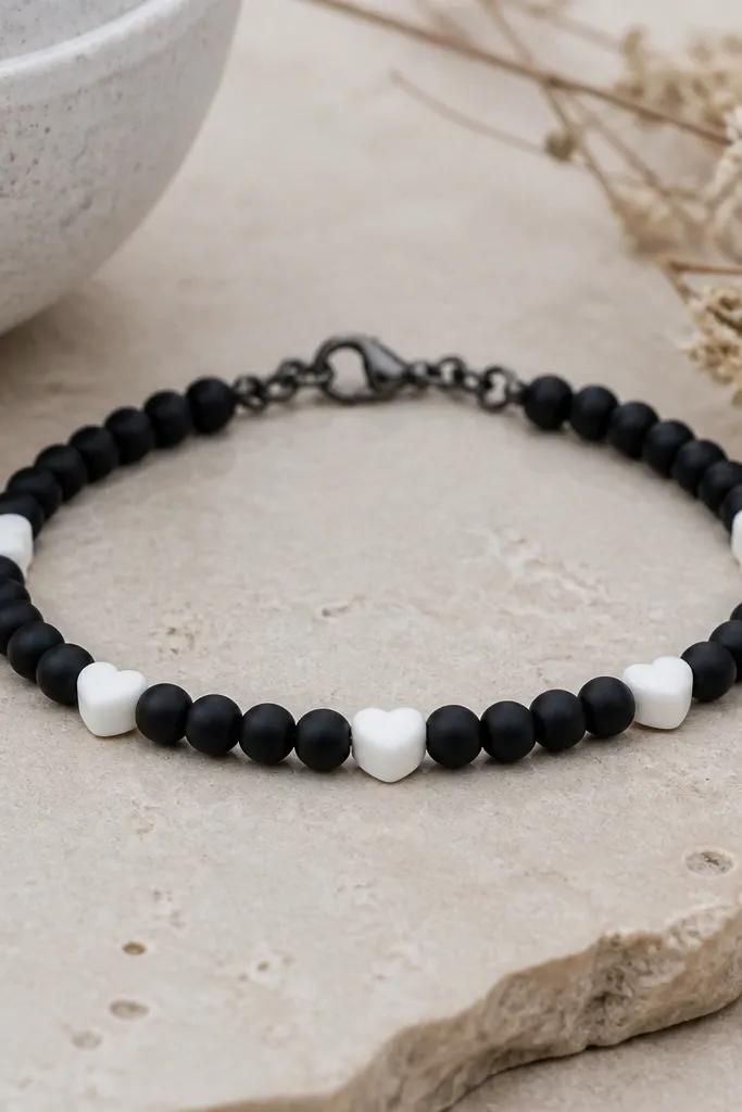 A bracelet with matte black clay beads (6mm) and a few small white clay heart beads spaced evenly. The hearts face the same direction on the front. The clasp is blackened silver.