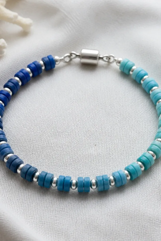 A bracelet with ocean blue clay beads that fade from deep navy to lighter teal. Small 3mm silver spacers sit between the beads. The clasp is a silver barrel clasp with a clean, minimal profile.