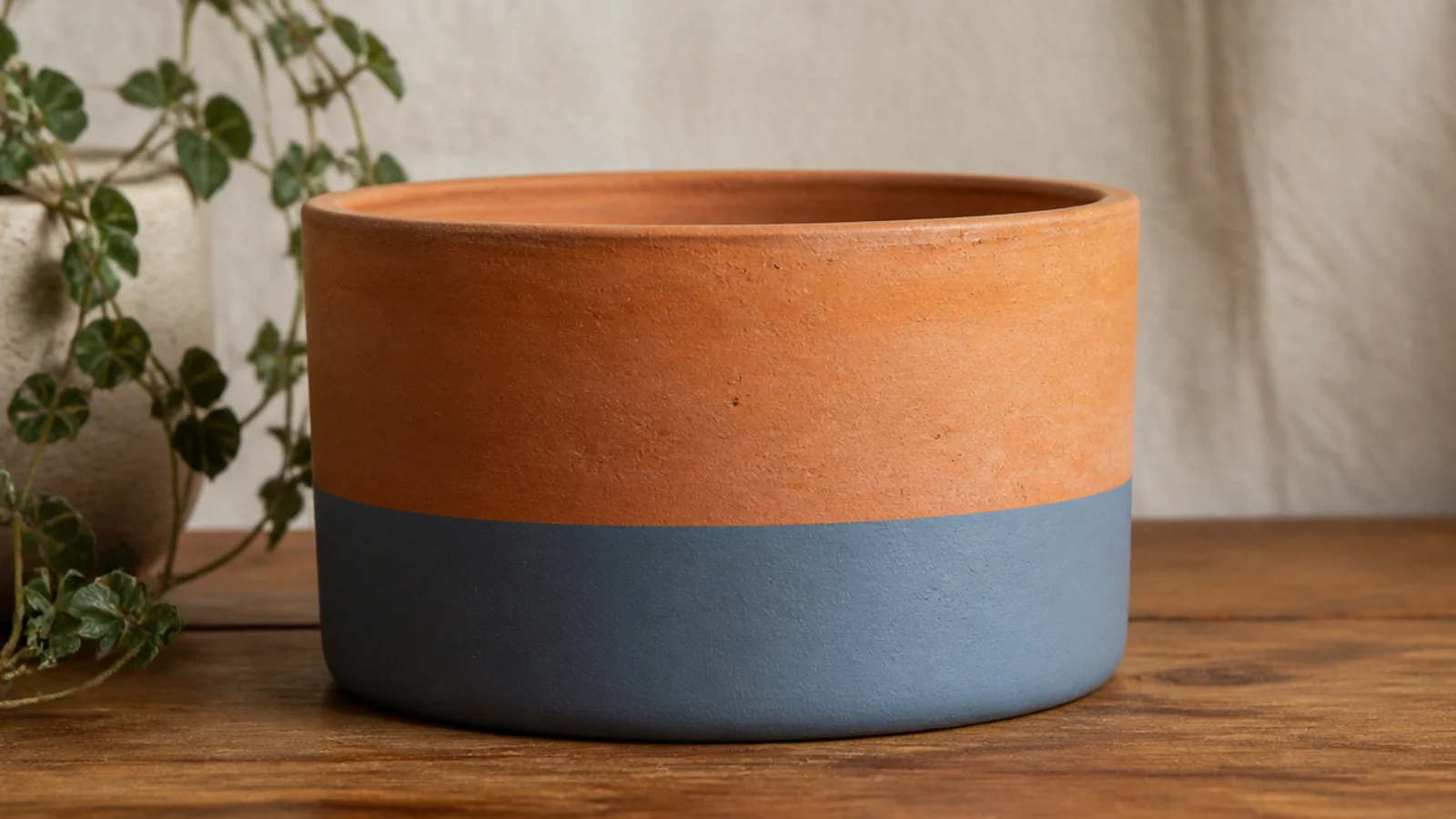A natural clay pot with the bottom third painted a clean band of dusty blue, the top left as bare terracotta.