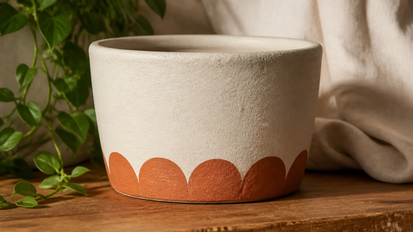 A cream clay pot with a row of evenly sized half-circle scallops painted in terracotta along the bottom edge.