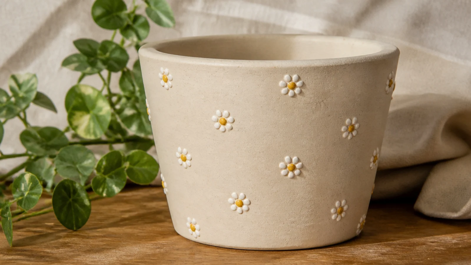 A cream clay pot decorated with small five-dot daisies, each flower white petals around a yellow center, scattered around the body.