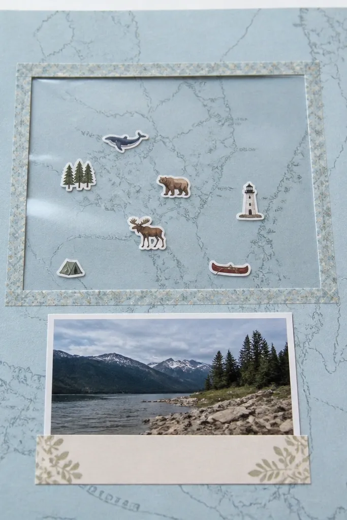 A light blue page with a printed map background. A clear acetate window sits in the center, framed by a thin strip of washi tape. Under the acetate, small sticker icons mark places. A photo sits below the window with a caption strip.