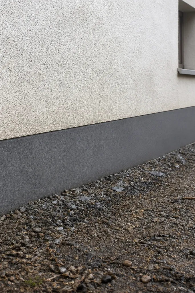 Compound wall with a darker, sealed base band and clean upper plaster