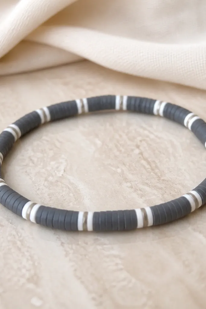 A charcoal gray clay bead bracelet with two-tone white mini disc beads in between; the pattern is simple, clean, and evenly spaced.