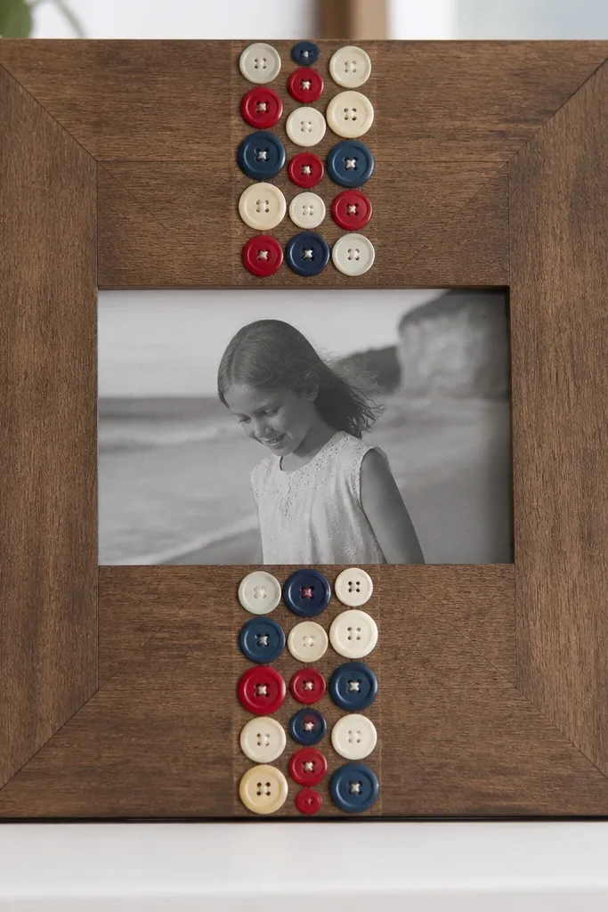 A wood frame with a vertical stripe in the middle made from sewn-on buttons in cream, navy, and red, with buttons varying in size and a neat grid spacing.