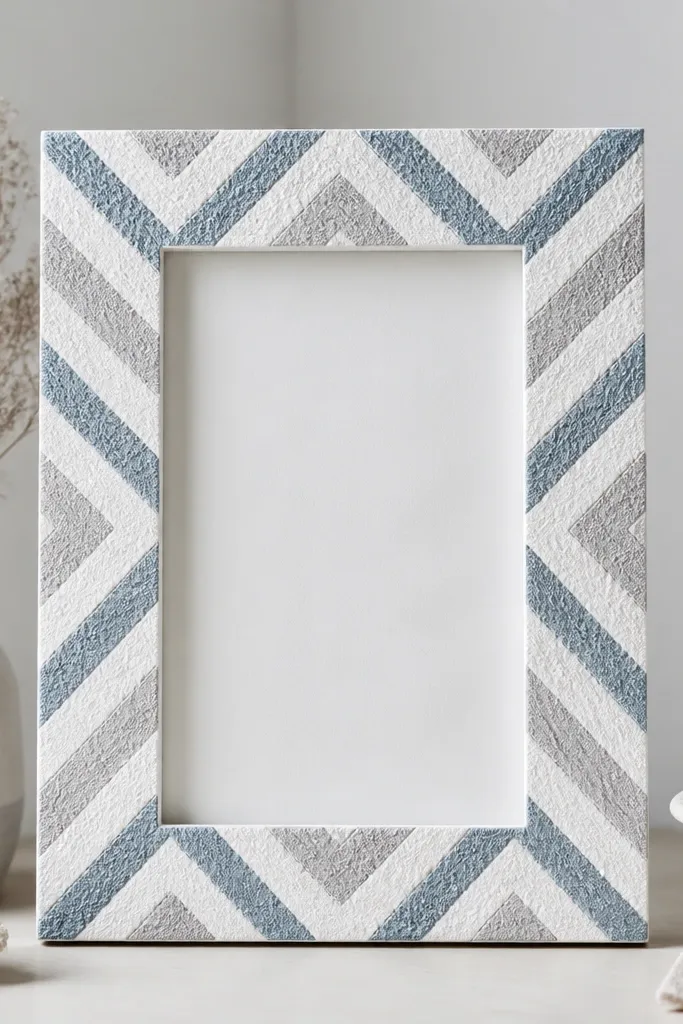 A white frame with a chevron pattern painted in dusty blue and light gray, with a rough salt-textured finish on the paint lines.