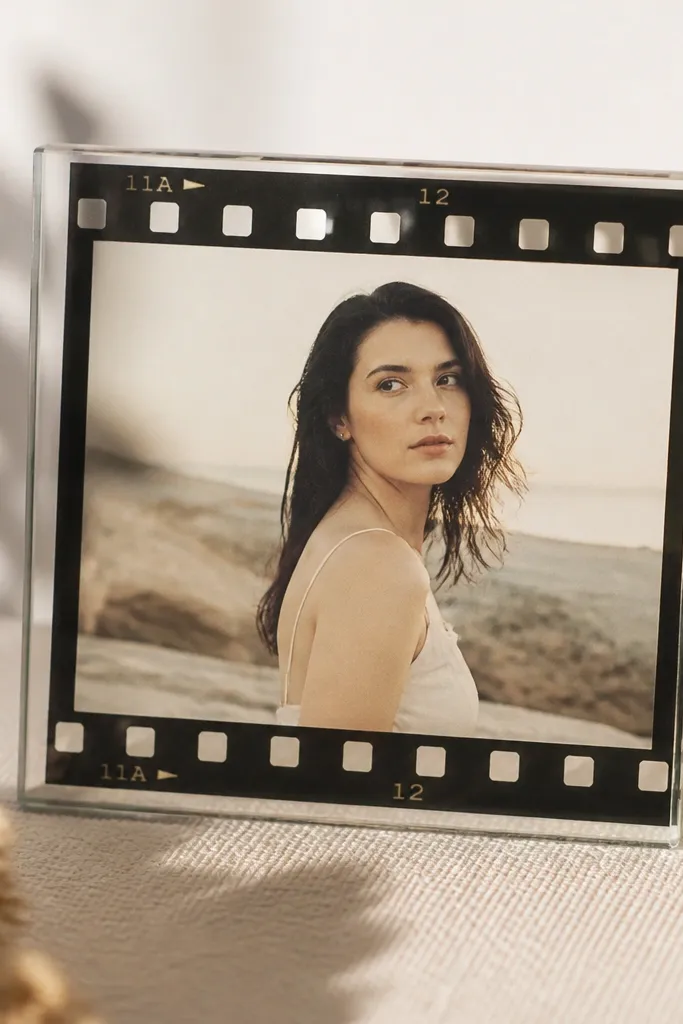 A frame with a clear outer layer where printed film strip graphics are glued along the border, showing sprocket holes and tiny numbers, with the photo visible through.