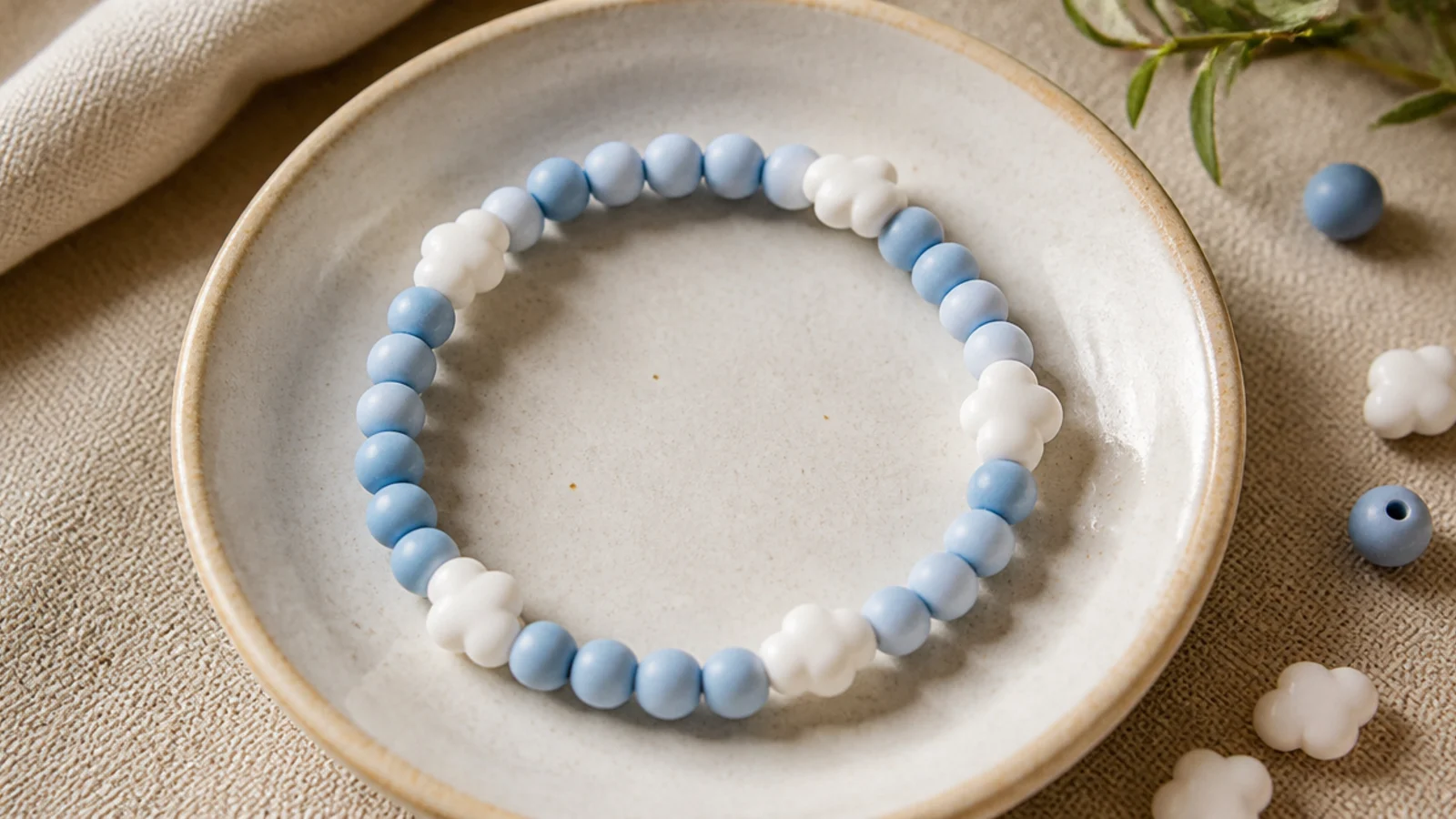 A sky-blue clay bead bracelet with a few small white puffy cloud-shaped beads spaced around it.