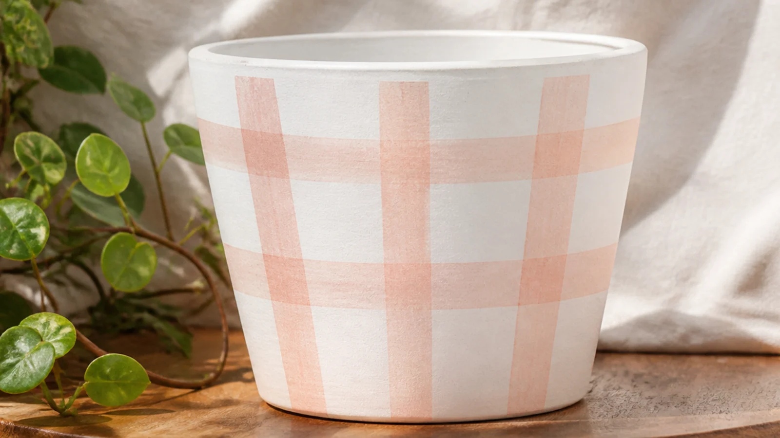 A white pot with a soft blush gingham pattern of overlapping translucent stripes forming a picnic-check grid.