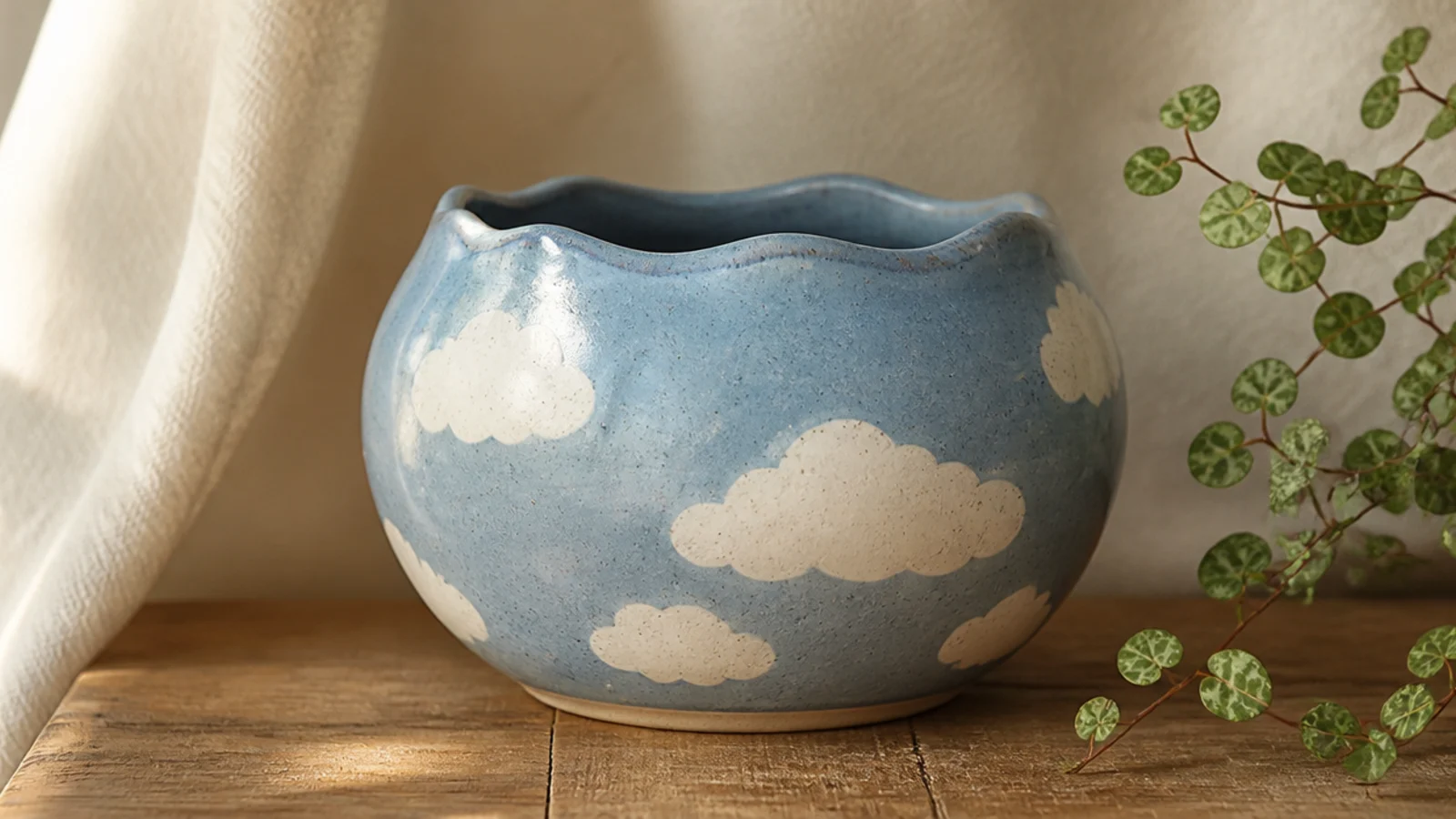 A soft blue pot with a few white puffy clouds painted around the body, simple rounded bumpy shapes.