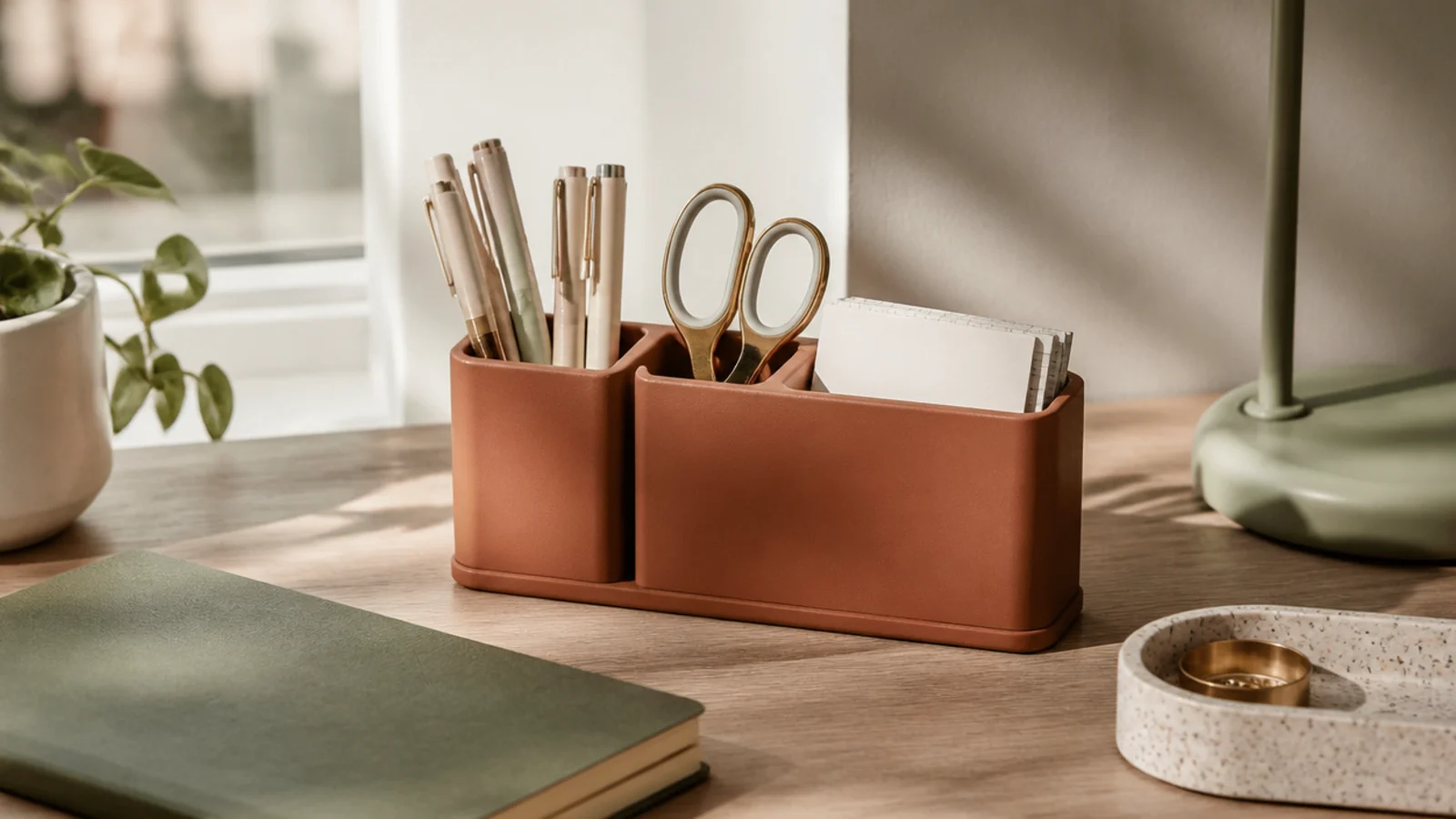 A compact desktop caddy with three sections holding pens, scissors, and sticky notes, sitting in the corner of a desk.