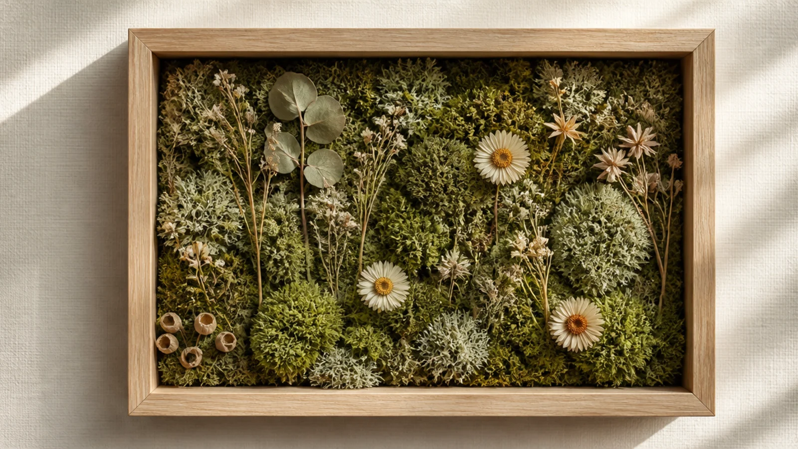 A shadow box with a bed of soft green preserved moss and a few dried flowers nestled into it, forest-like.