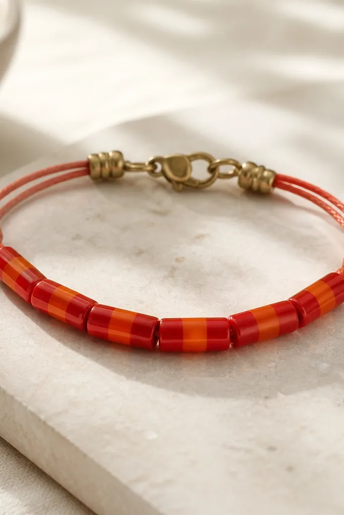 A bracelet with glossy-looking tube beads. The tubes have stacked red and orange bands, like soda candy. The bracelet uses red-orange cord and has small brass crimp beads near the clasp.