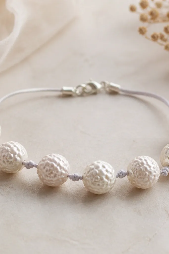 Round beads with raised bubble-like texture. The clay is a soft white with a faint pearly sheen. The bracelet looks airy, using thin satin cord and a small clasp.