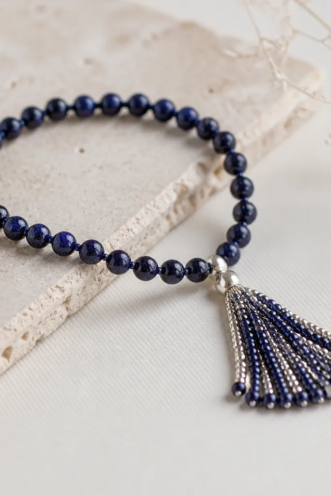 A bracelet with small round galaxy beads and a fringe detail on one end. The fringe is made from tiny seed beads in silver and dark blue, hanging from a single connector bead.