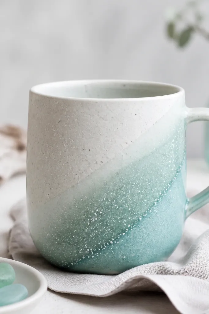 A mug with a diagonal sea-glass swoosh in mint and aqua, plus tiny white speckles like salt spray.