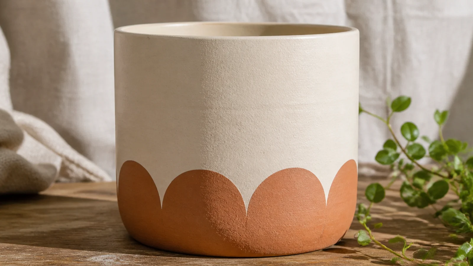 A cream pot with a row of evenly sized half-circle scallops painted in terracotta along the bottom edge.