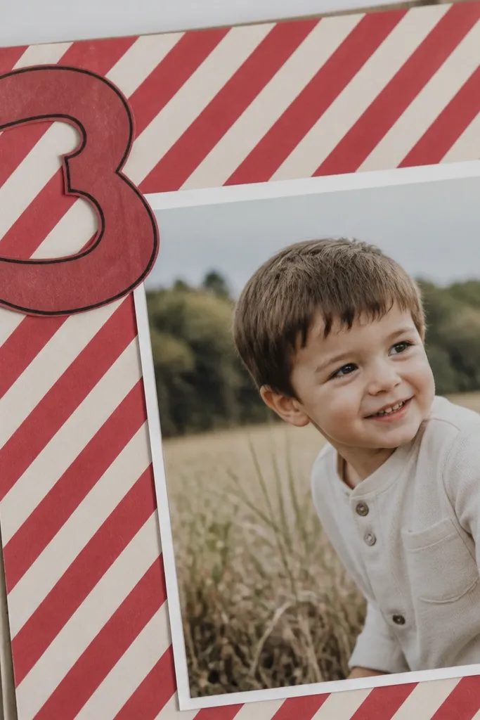 A page with diagonal red and white stripes behind a photo; a large number in the corner is cut from cardstock and outlined with black pen.