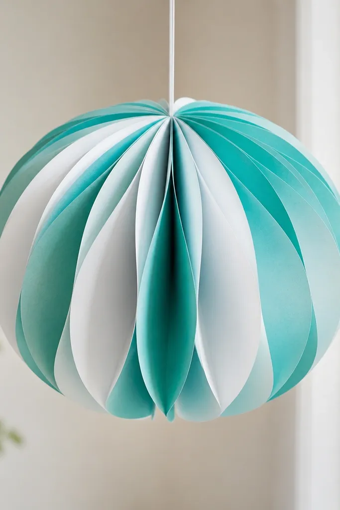 A hanging tissue flower globe with multiple paper layers radiating from a central knot. The outer petals are semi-circular and create a lantern look. Colors are teal and white with a crisp, symmetrical shape.