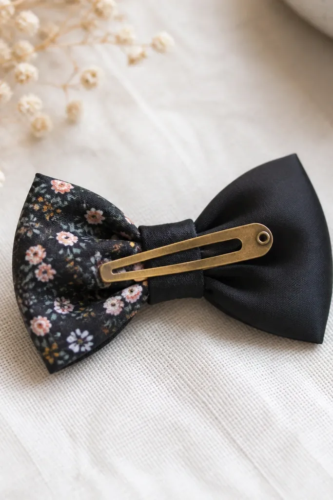A small fabric bow made from two patterns (tiny florals and solid black) with a snap clip attached on the back; the bow edges are turned in and look neat.