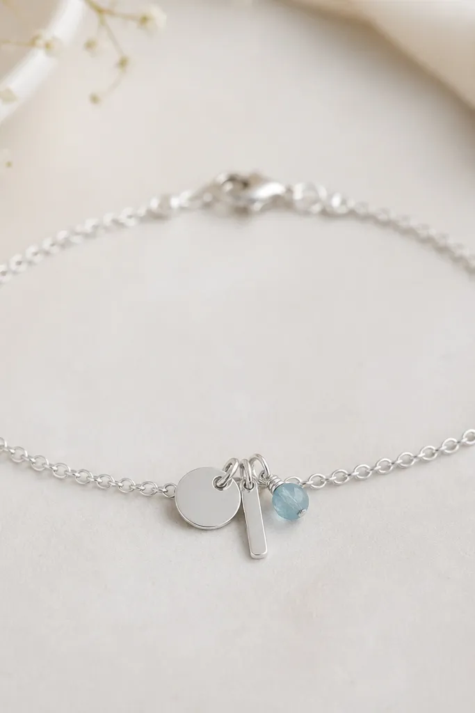 A delicate bracelet with three stacked charms: a small circle, a tiny bar, and one single birthstone bead. The bracelet is silver-toned with a simple clasp.