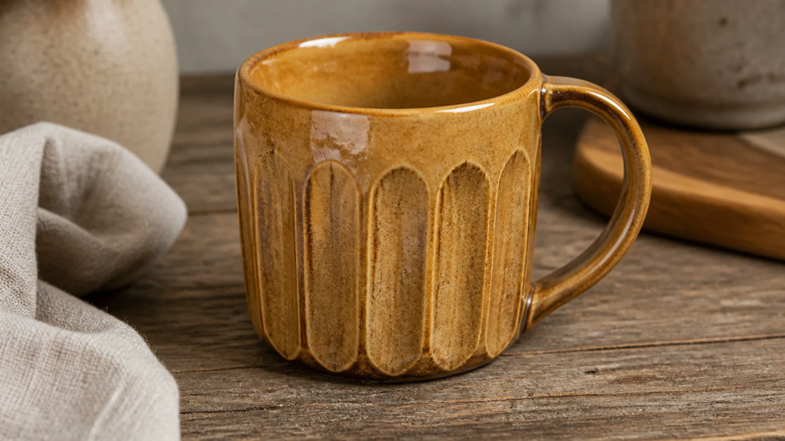 A coffee mug with flat carved facets cut vertically around the body for grip, glazed in glossy honey-amber that pools in the cut edges, on wood.
