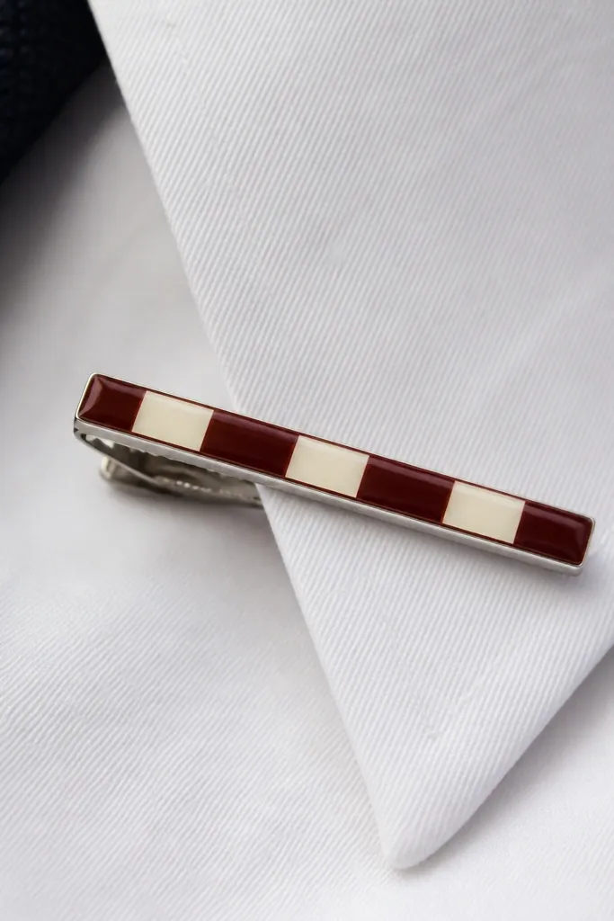 A metal tie clip painted with a small hand-painted stripe pattern in burgundy and cream, finished with a glossy clear coat; it sits on a white shirt collar.