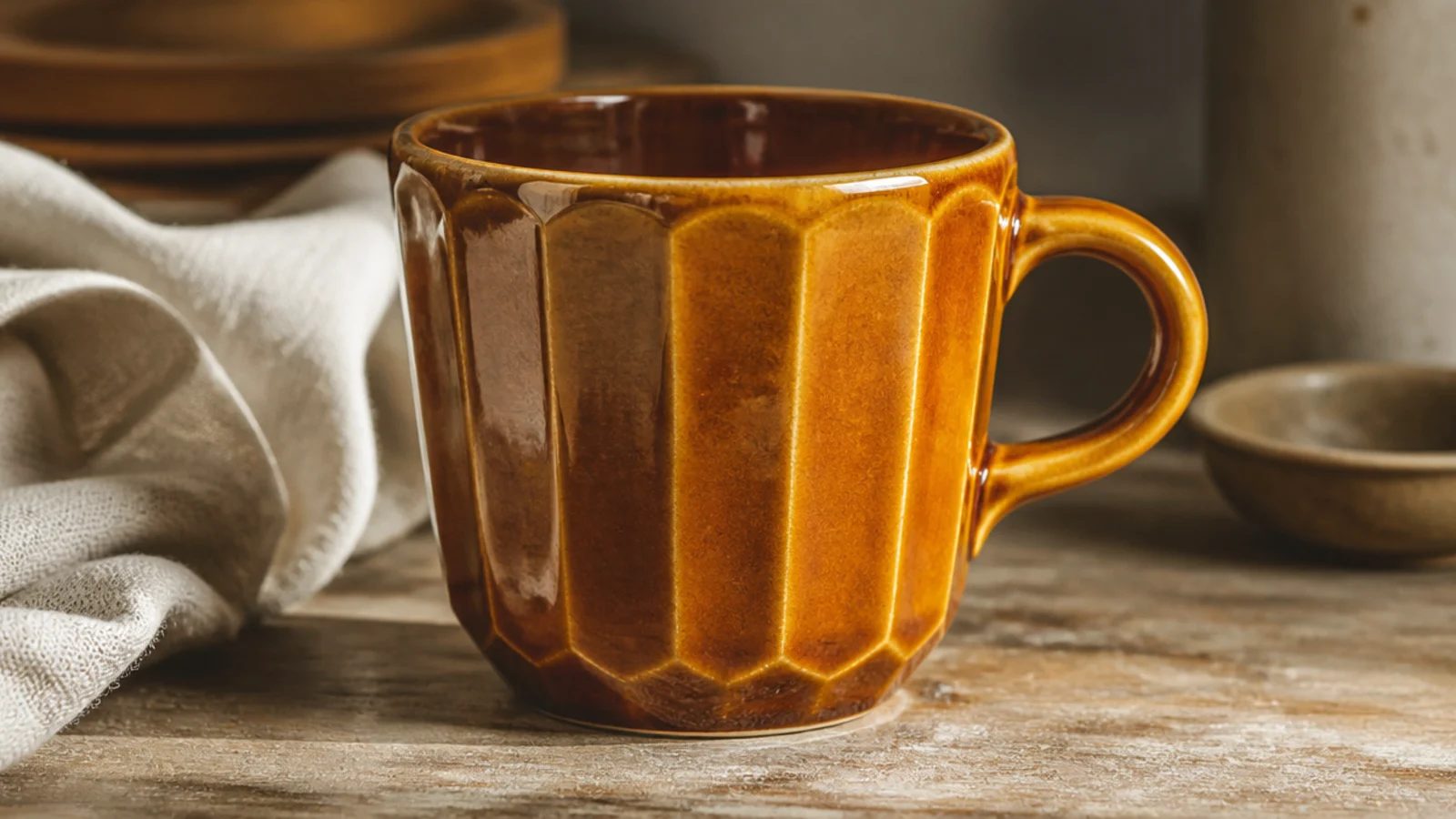 A mug with flat carved facets cut vertically around the body making a faceted gem-like surface, glazed in glossy amber.