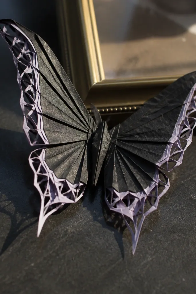 Black butterfly with crisp wing folds that show lighter paper edges