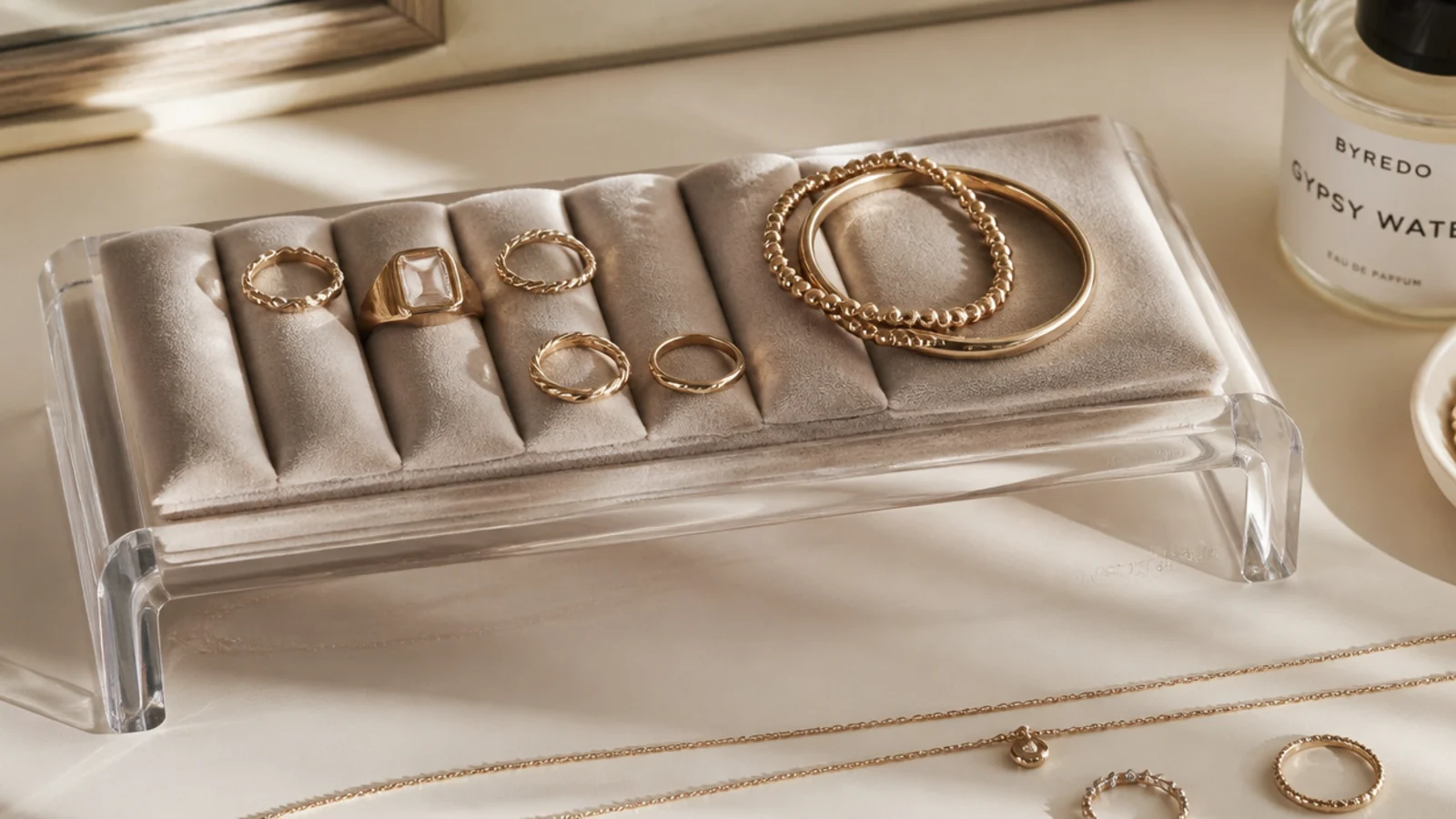 A minimalist clear acrylic riser on a vanity holding a folded velvet pad with rings and a couple of bracelets.