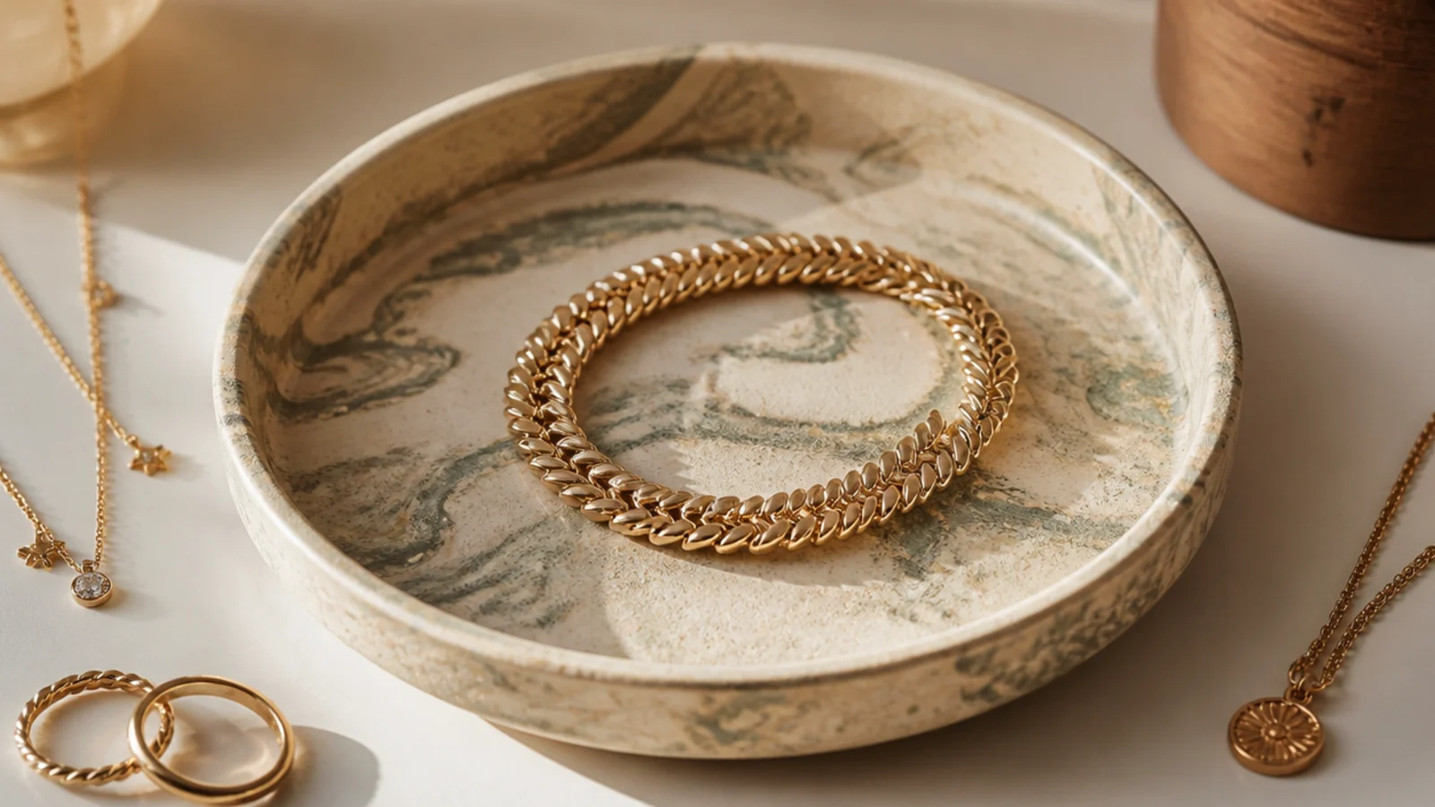 A shallow clay dish with cream and sage marbled swirls throughout the clay body, holding a coiled bracelet.