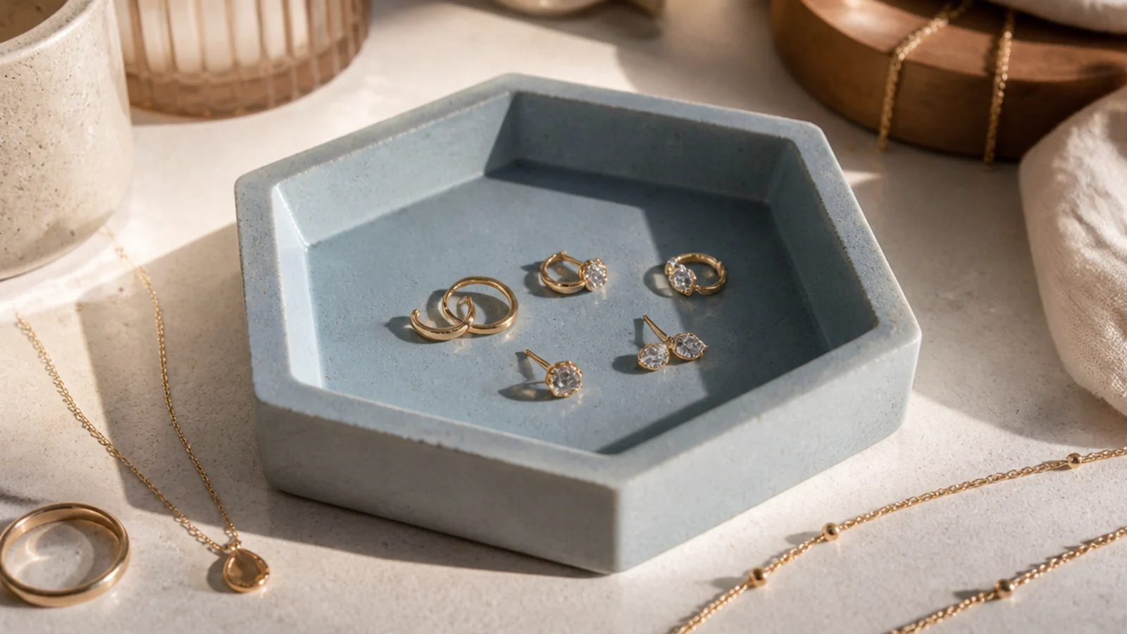 A dusty-blue clay dish with flat angular faceted sides forming a hexagonal bowl, holding studs and small rings.